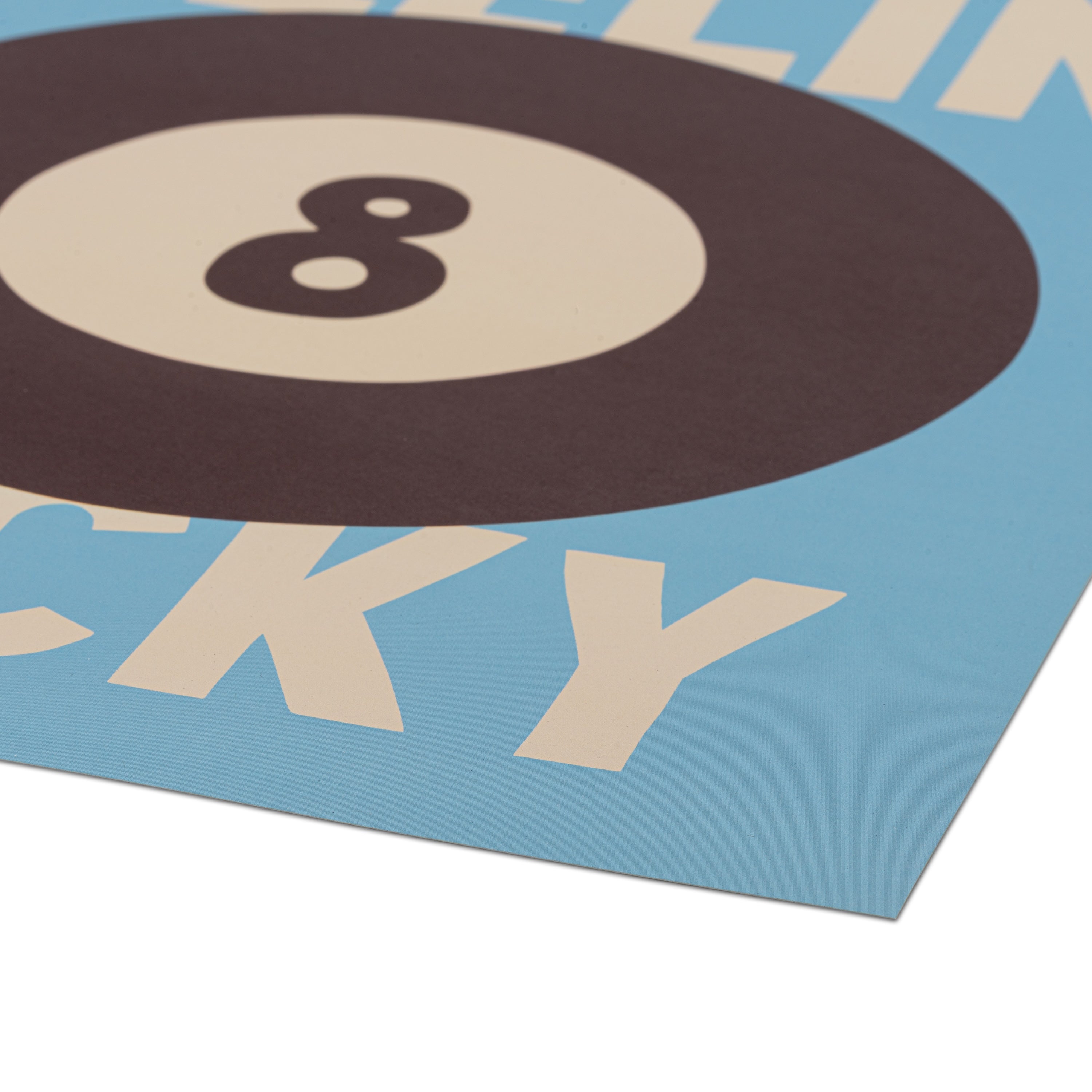A close-up of a printed poster corner showing large cream lettering on a light blue background, with a dark maroon 8-ball at the top and a white underneath.